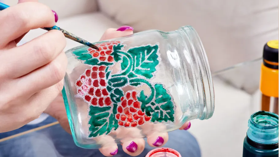 Person malt Glas mit Beerenmotiv.