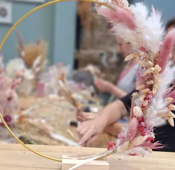 Floral wreath on table, hands arranging flowers.