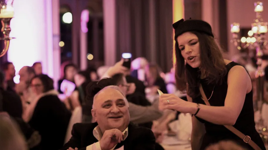 Woman talking to seated man at event.