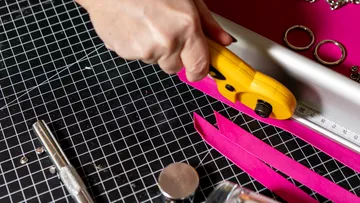 Hand cutting pink paper on cutting mat.
