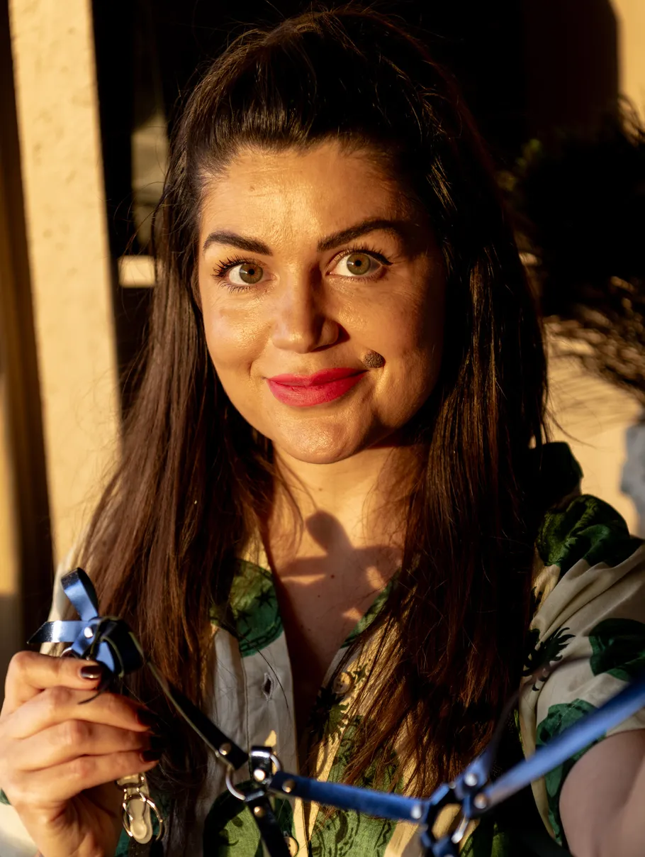 Woman smiling holding blue harness indoors.