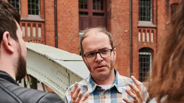 Man talking with two people outside brick building.