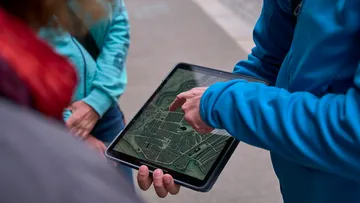 Person pointing at map on tablet outdoors.