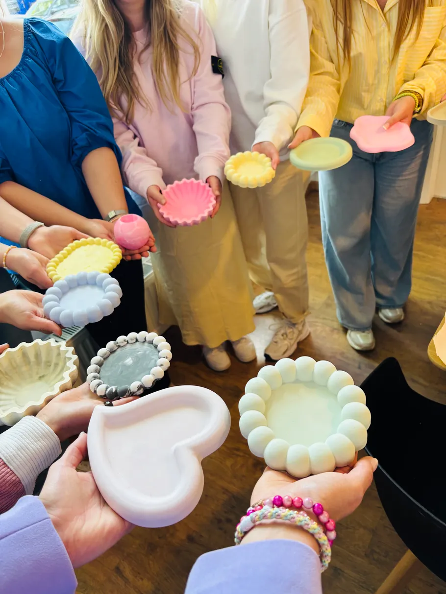 Women hold colorful clay trays indoors.