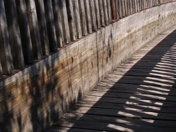 Holzsteg verläuft entlang einer hölzernen Wand im Schatten.