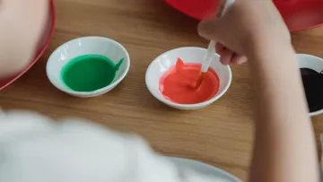Child painting with colored paints on table.