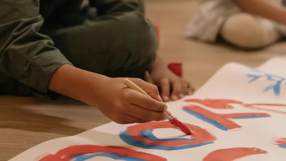 Child painting letters on paper indoors.