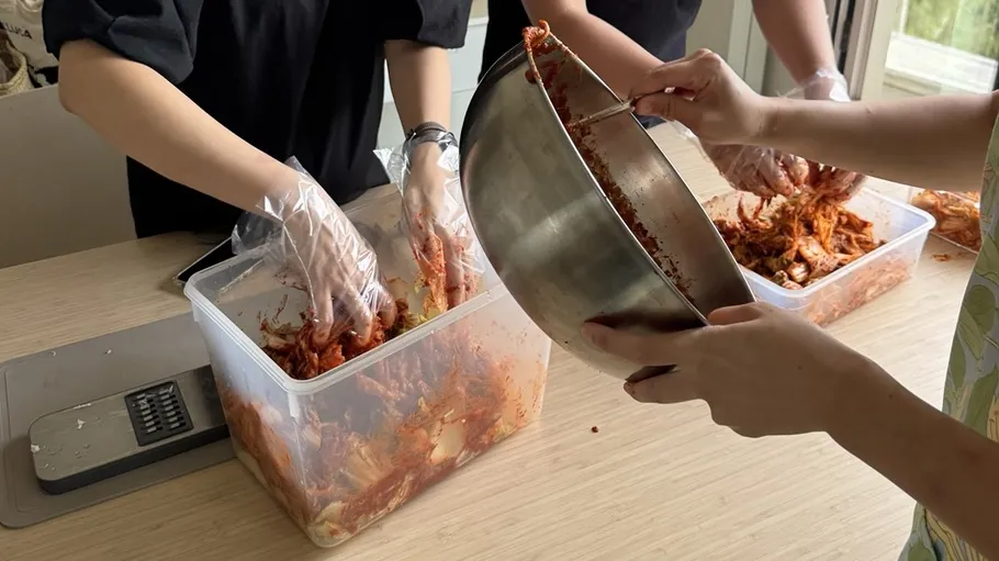 People making kimchi with gloves indoors.
