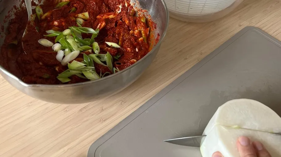 Hand chopping radish, bowl of kimchi nearby.
