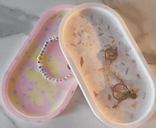 Two trays with jewelry on a marble surface.