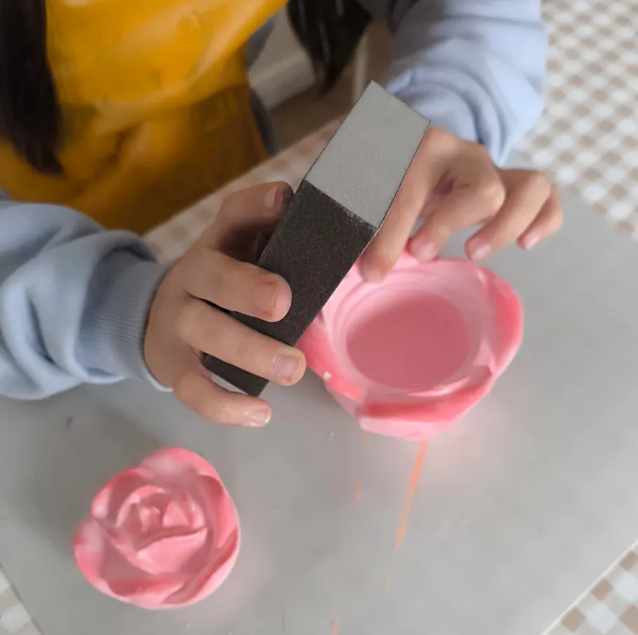Person sanding pink soap flower on table.