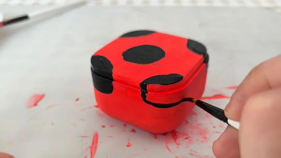 Rote Schachtel mit schwarzen Punkten bemalt.