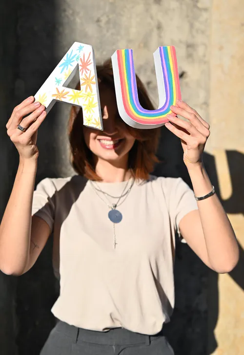Frau hält bunte Buchstaben 'A' und 'U' draußen.