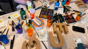 Bastelmaterialien und bemalte Buchstaben auf Tisch.