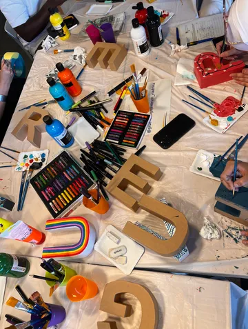 People painting cardboard letters at a table.