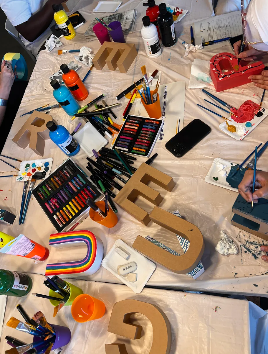 People painting letters on a cluttered table.