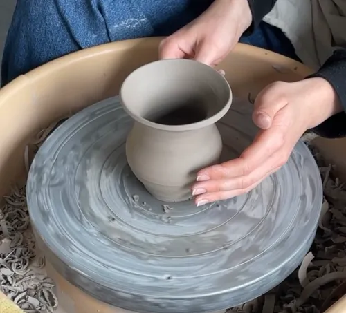 Hands shaping clay pot on pottery wheel.