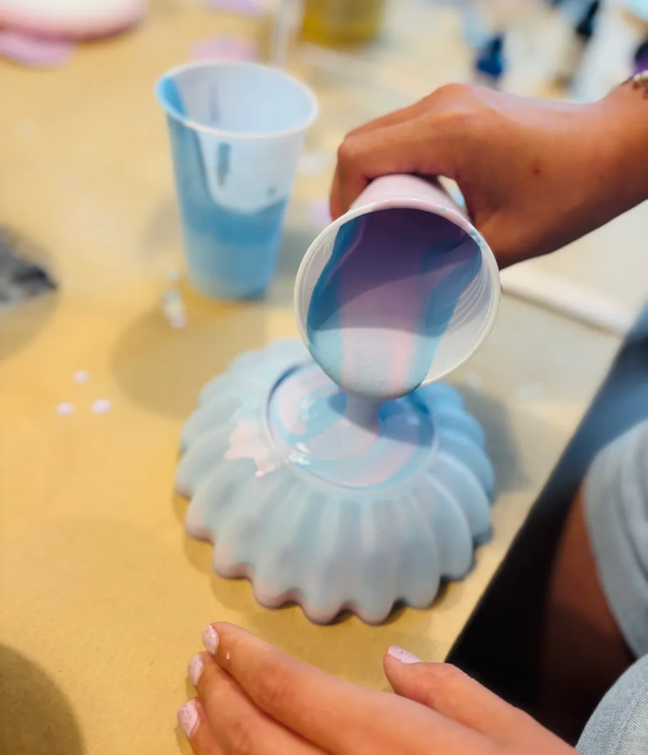 Hand pours blue paint onto decorative mold.