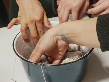 Several hands reach into a pot of ingredients.