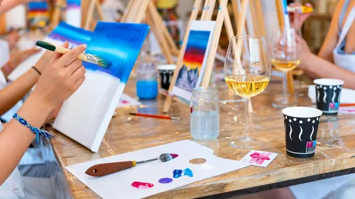 Person painting with wine glass nearby.