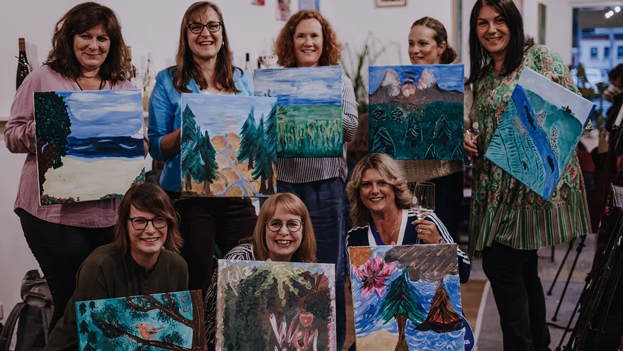 Women holding painted canvases in a studio.