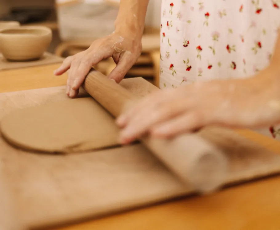 Person rollt Ton auf Holzbrett.