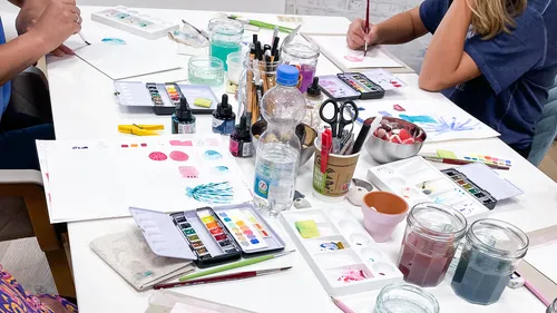 Leute malen mit Aquarellkästen am Tisch.