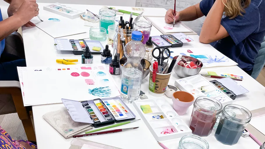 Leute malen mit Aquarellkästen am Tisch.