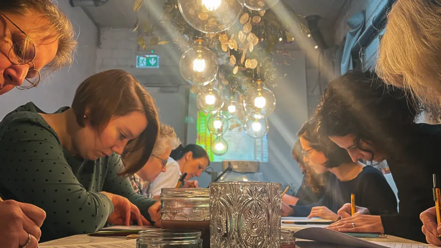 People writing at a long table under hanging lights.