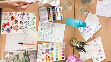 Art supplies and watercolor paintings on table.