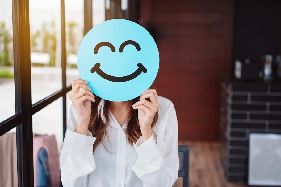 Person hält Smiley-Gesicht im Büro.