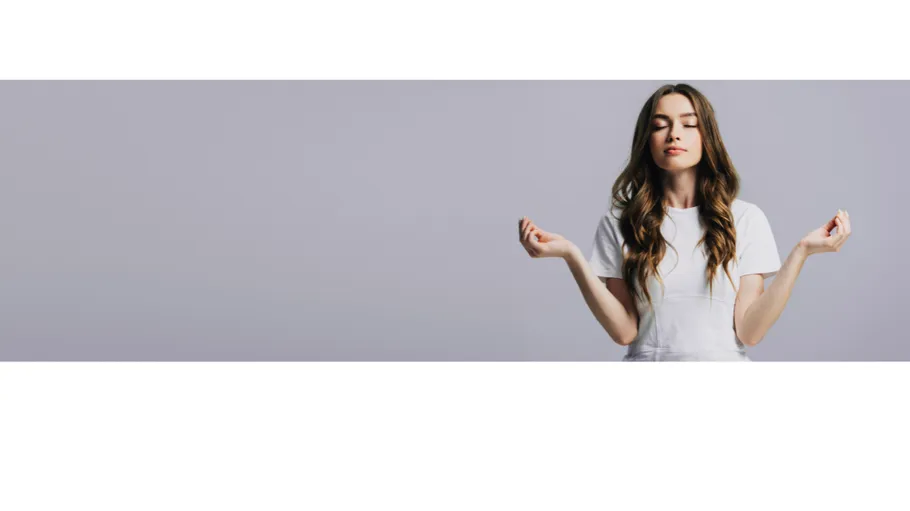 Woman meditating in white shirt, neutral background.