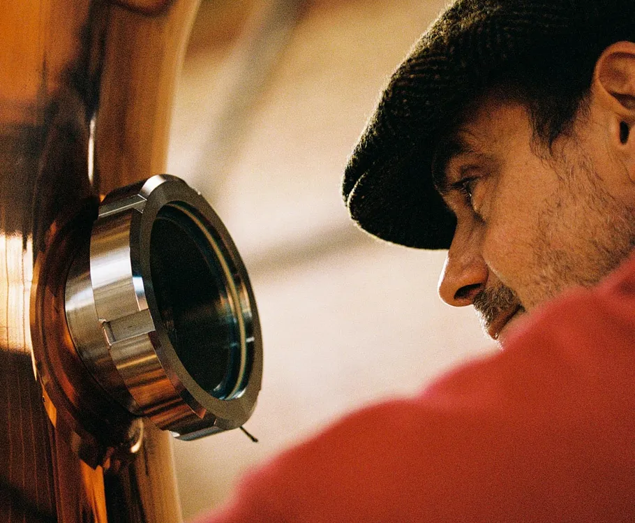 Man inspecting distillery equipment closely indoors.