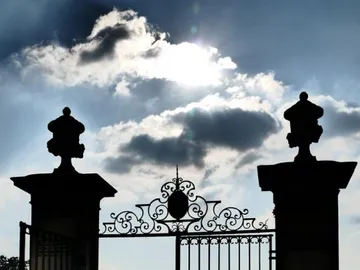 Eingangstor mit dekorativen Säulen, silhouettiert gegen Himmel.