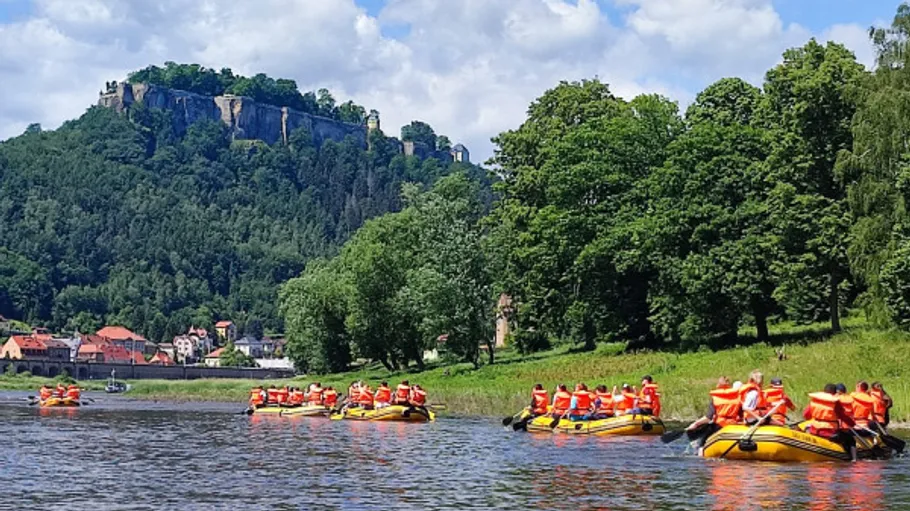 Gruppen beim Rafting auf Fluss nahe bewaldetem Hügel.