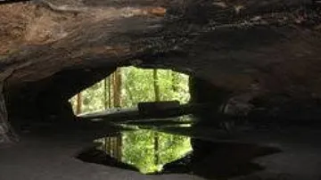 Cave opening with forest reflection in water.