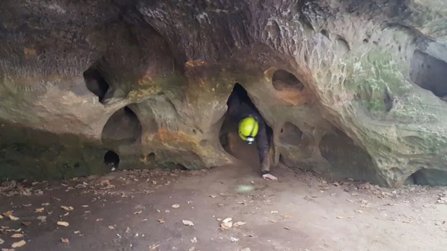 Person kriecht aus einer Felshöhle.
