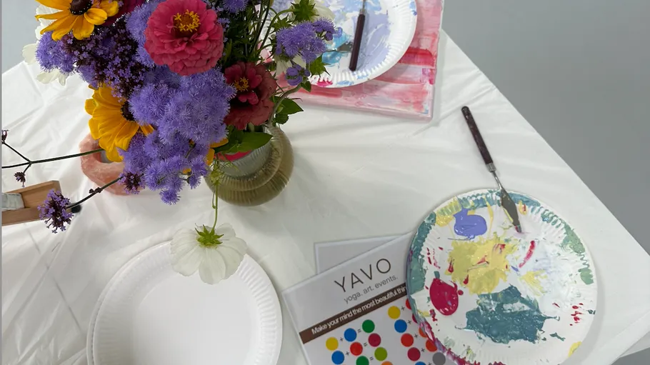 Flowers in vase, paint palette, art supplies table.