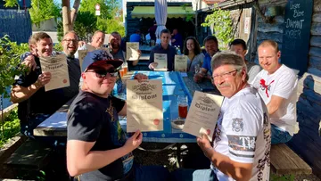Group smiling with certificates at outdoor table.
