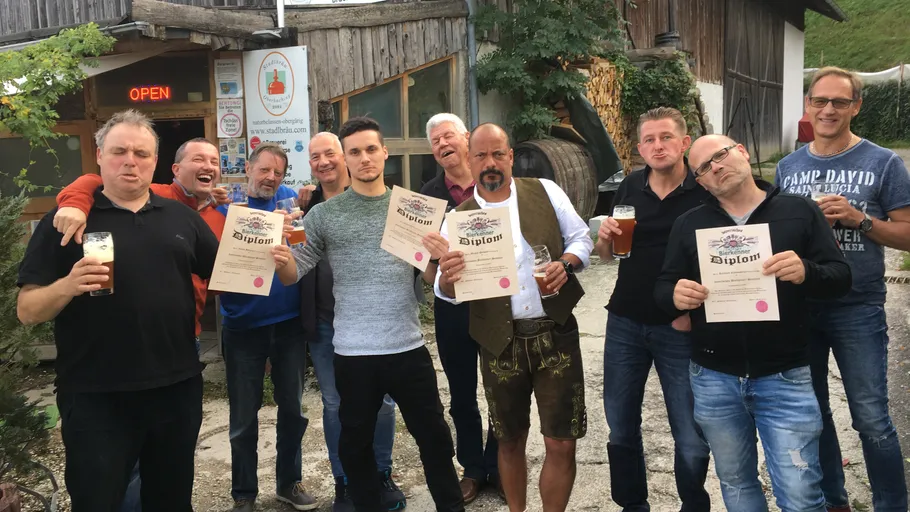 Group of men holding beer diplomas outside building.