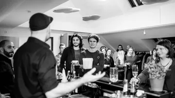 Personen versammelt um eine Bar im Gespräch.