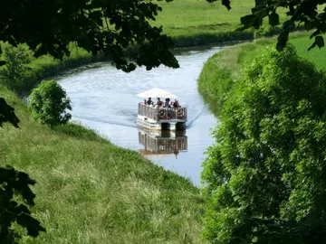 Eine Fähre fährt auf einem ruhigen Wasserweg durch grüne Landschaft.