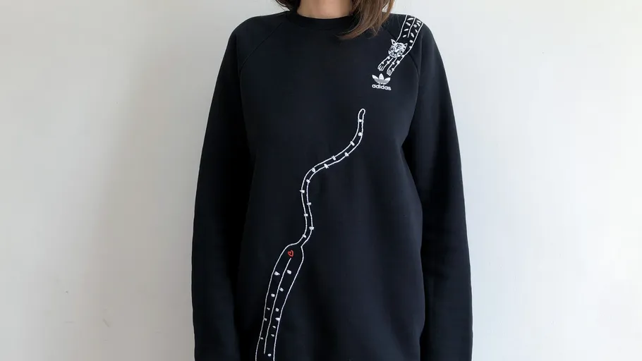 Person trägt schwarzen Pullover mit Schlangenmuster.