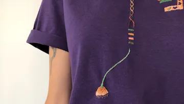 Lila Shirt mit buntem Stickdetail.