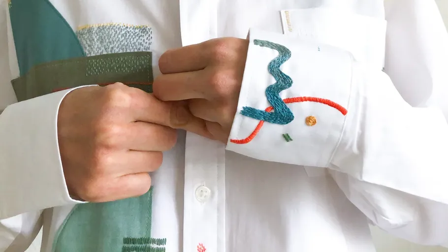 Hands adjusting abstract embroidered shirt.