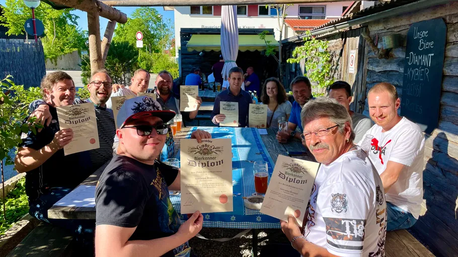 Group holding beer diplomas at outdoor table.