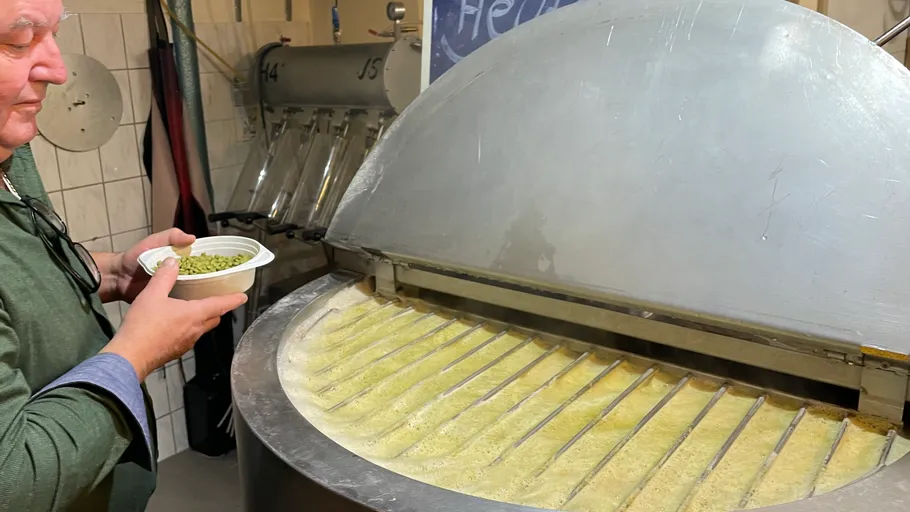 Man holding bowl near large brewing equipment.