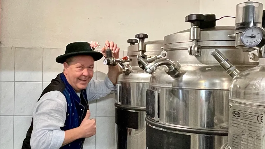 Man in hat operates brewing equipment, smiles.