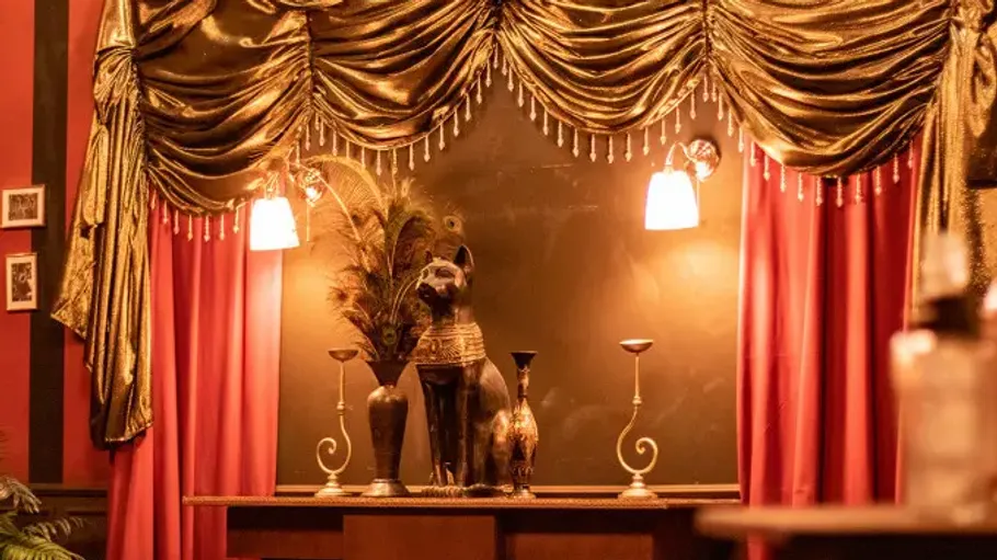 Statue and decor under draped gold curtains.