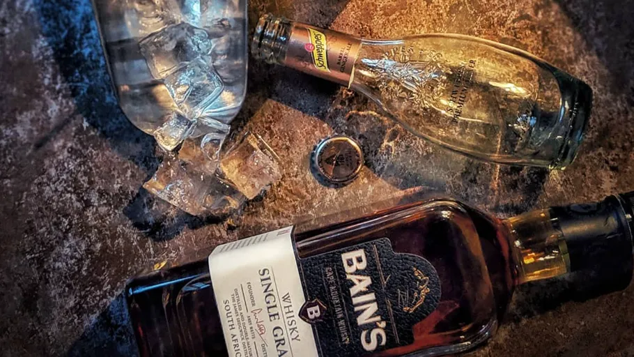 Bain's whiskey and Schweppes bottle with ice cubes.
